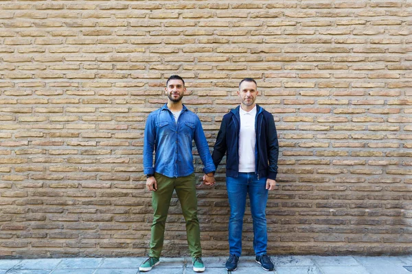 Gay coppia tenendo mani posa di fronte a un mattone muro. — Foto Stock