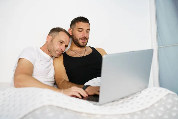 Gay paar consulting iets op hun laptop terwijl liggend op het bed. — Stockfoto