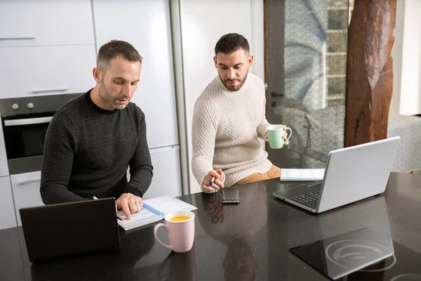 Pareja gay trabajando juntos en casa con sus computadoras portátiles. —  Fotos de Stock