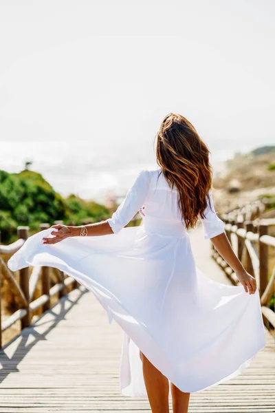 Young woman wearing a beautiful white dress in Spanish fashion on a boardwalk on the beach. — Stock Photo, Image