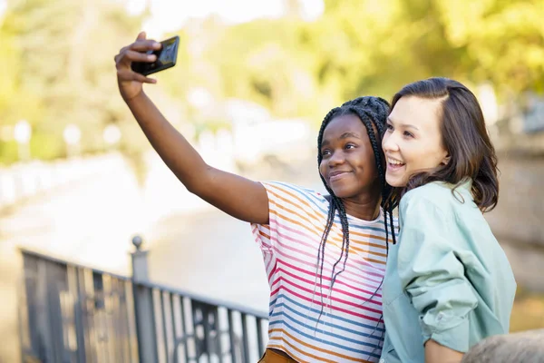 Dwie wielonarodowe przyjaciółki robiące selfie na świeżym powietrzu. — Zdjęcie stockowe