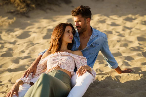Привлекательная пара, сидящая на песке пляжа и наслаждающаяся друг другом — стоковое фото