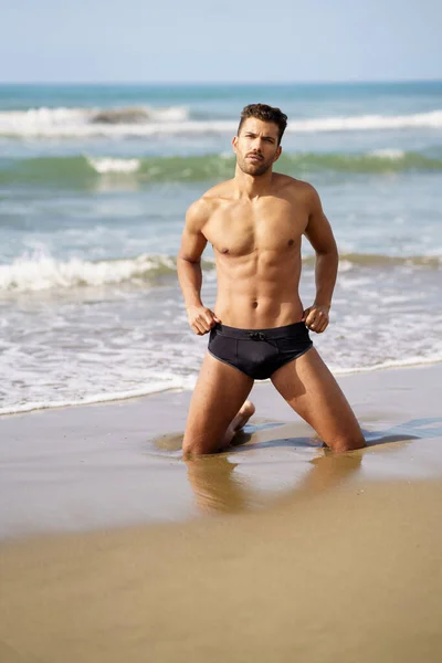 Beau homme à genoux sur le sable de la plage — Photo