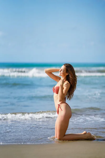 아름다운 몸으로 해변 모래 위에 무릎을 꿇고 있는 여인 — 스톡 사진