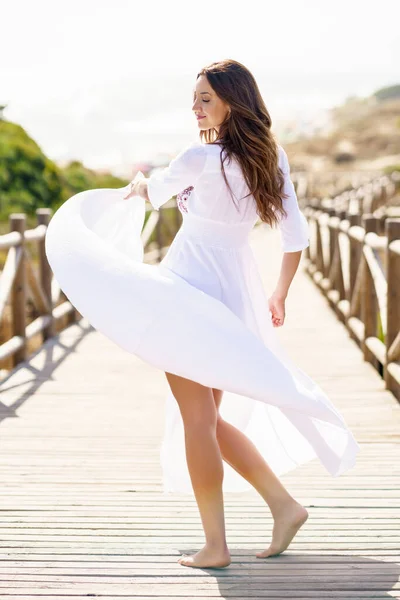 아름다운 흰색 드레스를 입은 젊은 여자가 스페인식으로 해변에서 보드 워크를 하고 있다. — 스톡 사진