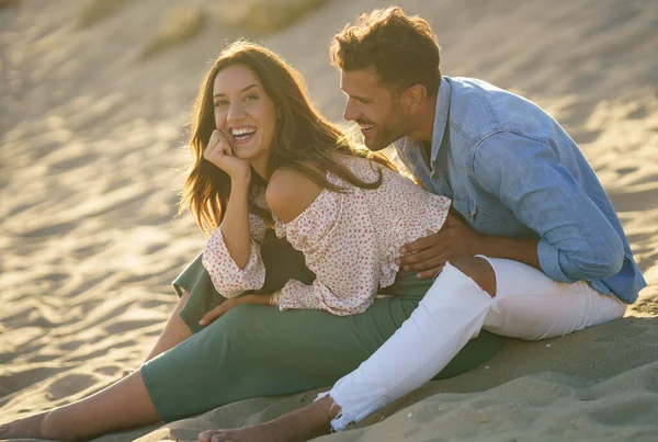 Casal jovem rindo juntos sentados na areia da praia — Fotografia de Stock