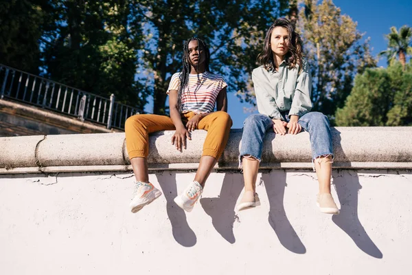 İki çok ırklı kadın bir şehir duvarında oturuyor.. — Stok fotoğraf