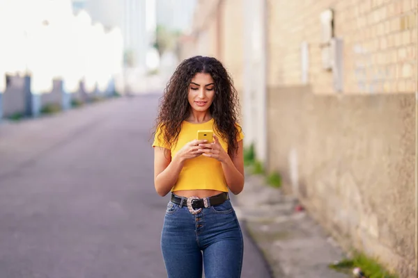 Genç bir Arap kadın akıllı telefonuyla sokakta yürüyor. — Stok fotoğraf