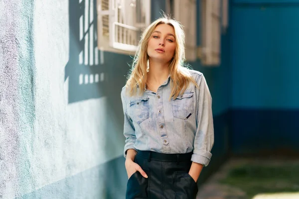 Blonde woman wearing denim shirt and black leather skirt standing in the street. — Stock Photo, Image