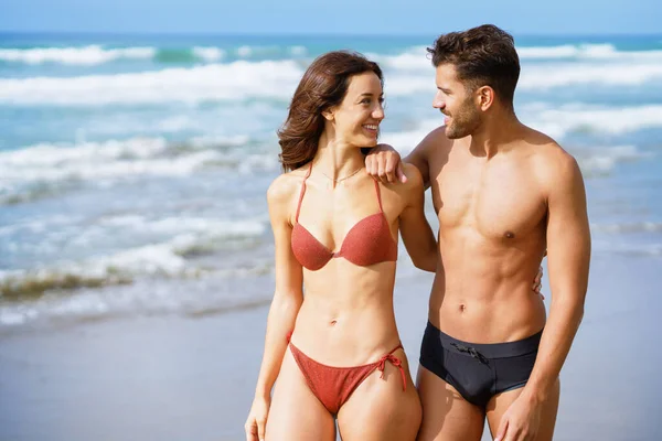 Ein junges Paar schöner athletischer Körper, die zusammen am Strand spazieren gehen — Stockfoto