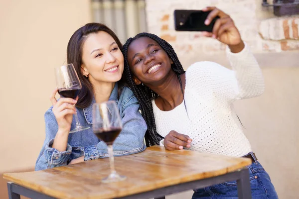 Två kvinnor som gör en selfie med en smartphone samtidigt som de dricker ett glas vin. — Stockfoto