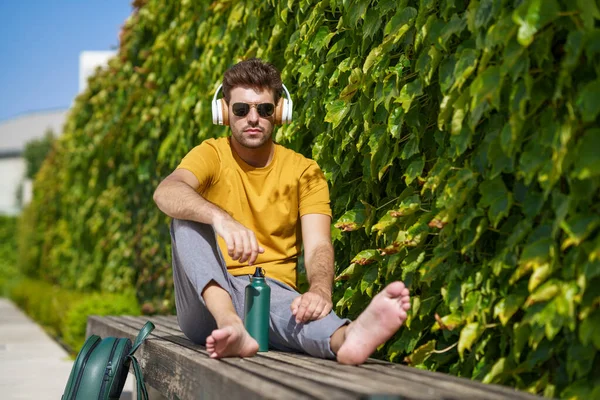 Man zit buiten met een aluminium waterfles, koptelefoon en rugzak. — Stockfoto