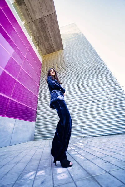 Wide-angle photo of a woman wearing blue suit posing near a modern building.