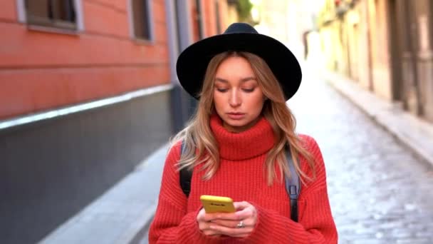 Blond vrouw praten op haar smartphone tijdens het lopen in de straat. — Stockvideo