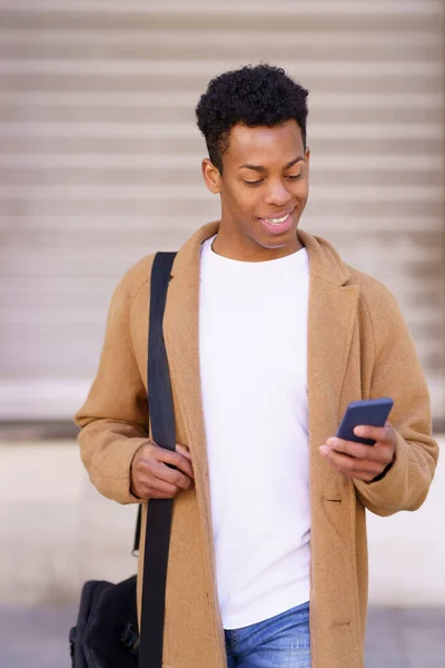 Smiling black man looking at his smartphone while walking down the street. — Stock Photo, Image