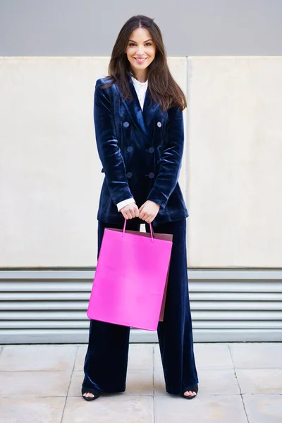 Mujer joven con traje azul llevando varias bolsas de compras cerca de un centro comercial. — Foto de Stock