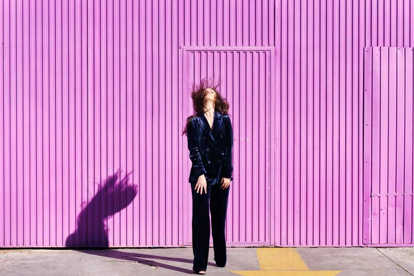 Woman wearing blue suit posing near pink shutter, moving her hair. — Stock Photo, Image