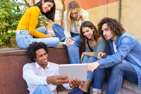 Multiethnische Gruppe junger Menschen, die im Freien vor urbanem Hintergrund ein digitales Tablet betrachten. — Stockfoto