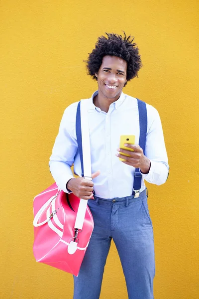 Černoch s afro účesem nesoucí sportovní tašku a smartphone ve žlutém pozadí. — Stock fotografie