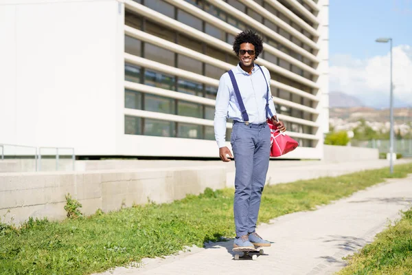 Černý podnikatel jízda na skateboardu v blízkosti administrativní budovy. — Stock fotografie
