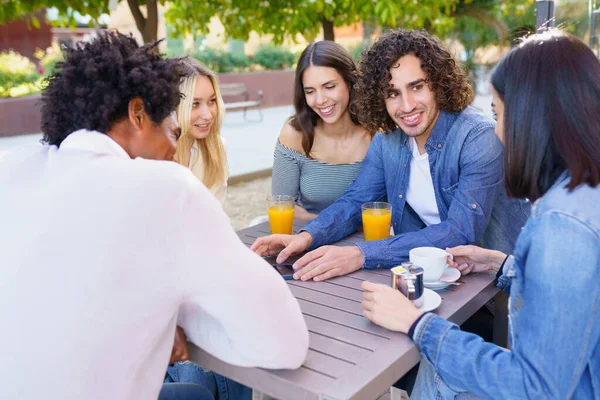 Tipo mostrando su teléfono inteligente a su grupo de amigos mientras toma algo en un bar al aire libre — Foto de Stock