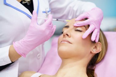 Estetik doktor orta yaşlı hastasının alnına botoks yapıyor..