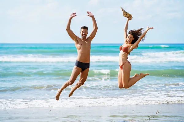 Lustiges junges Paar mit schönen Körpern springt an einem tropischen Strand. — Stockfoto