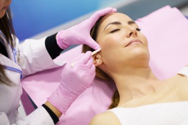 Doktor, PDO dikiş ipliklerinin enjekte edileceği kadınların yüzlerini boyuyor.