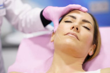 Doktor, PDO dikiş ipliklerinin enjekte edileceği kadınların yüzlerini boyuyor.