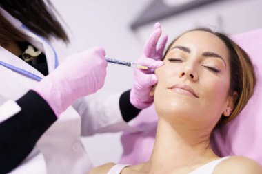 Doktor, yüz gençleştirme tedavisi için bir kadının elmacık kemiklerine hiyalüronik asit enjekte ediyor..
