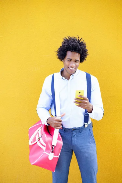 Černoch s afro účesem nesoucí sportovní tašku a smartphone ve žlutém pozadí. — Stock fotografie