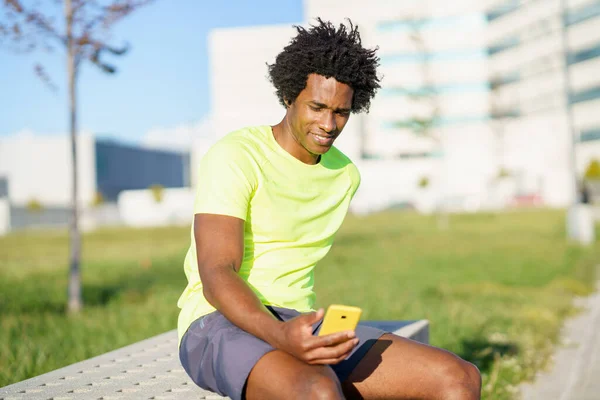 Schwarzer Mann konsultiert sein Smartphone mit einer Übungs-App, während er sich vom Training ausruht. — Stockfoto