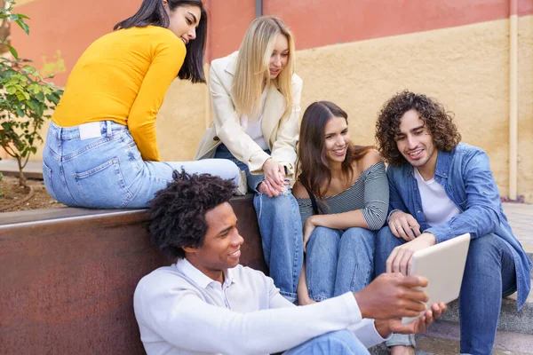 Grupo multi-étnico de jovens olhando para um tablet digital ao ar livre em fundo urbano. — Fotografia de Stock