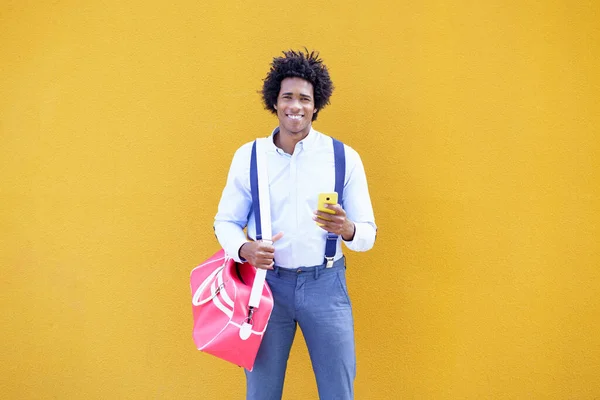 Černoch s afro účesem nesoucí sportovní tašku a smartphone ve žlutém pozadí. — Stock fotografie