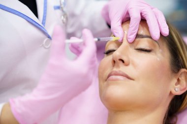 Estetik doktor orta yaşlı hastasının alnına botulinyum toksini enjekte ediyor..