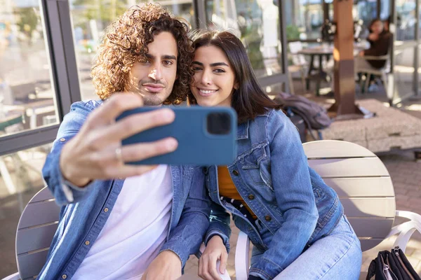 Pareja árabe tomando fotos selfie con su teléfono inteligente, sentado en la terraza de un bar. — Foto de Stock