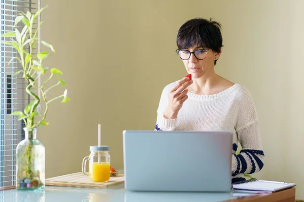 Mujer comiendo fresas mientras teletrabaja desde casa en su portátil —  Fotos de Stock