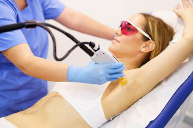 Woman receiving underarm laser hair removal at a beauty center. clipart