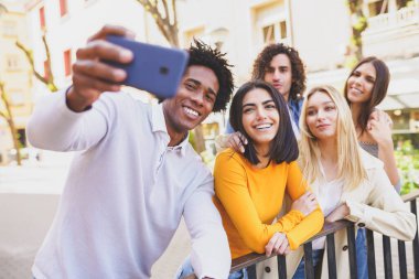 Çok ırklı bir arkadaş grubu akıllı telefonuyla sokakta selfie çekiyor..