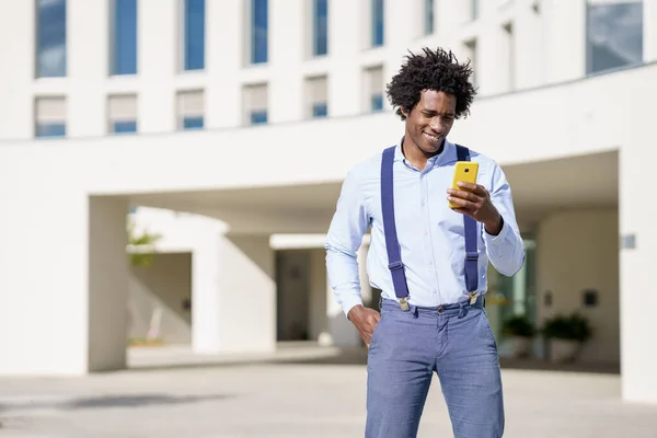 Uomo nero con acconciatura afro utilizzando uno smartphone vicino a un edificio per uffici. — Foto Stock