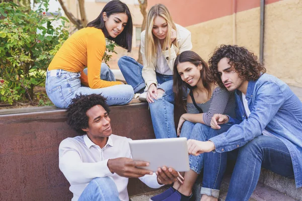 Multiethnische Gruppe junger Menschen, die im Freien vor urbanem Hintergrund ein digitales Tablet betrachten. — Stockfoto