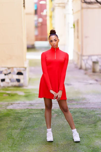 Ung svart kvinna i röd klänning poserar på en gata med färgglada väggar — Stockfoto