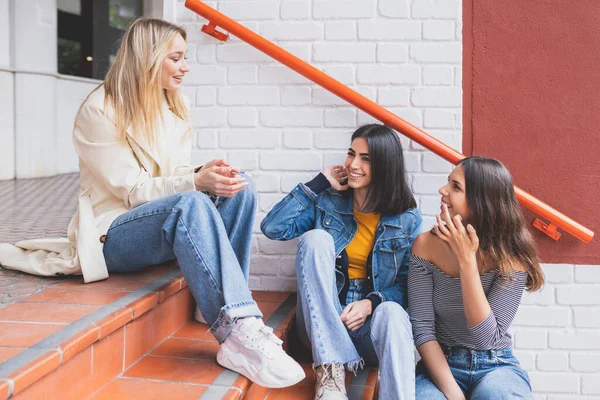 Gruppo multietnico di tre amici seduti sui gradini della strada che parlano. — Foto Stock