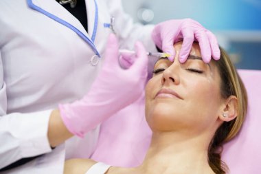 Estetik doktor orta yaşlı hastasının alnına botulinyum toksini enjekte ediyor..