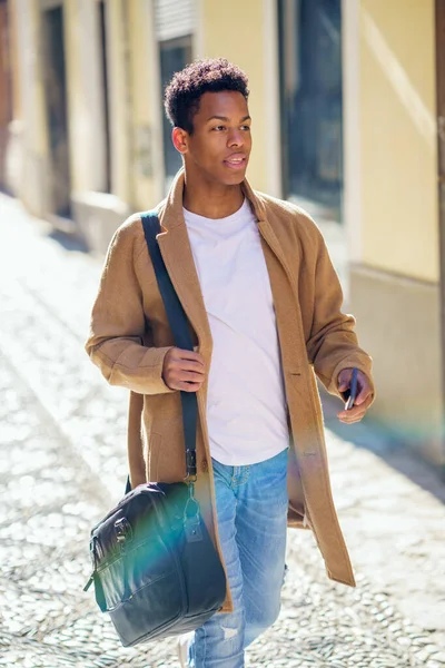 Giovane uomo nero che cammina per la strada con una valigetta e uno smartphone. — Foto Stock