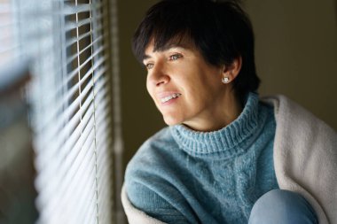 Pencereden bakarken gülümseyen orta yaşlı mutlu bir kadın..
