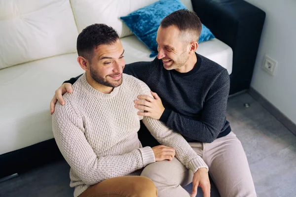 Pareja gay sentada cerca del sofá en casa en un momento romántico — Foto de Stock