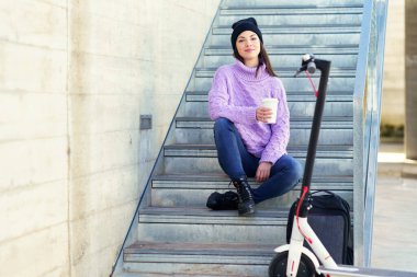 Elektrikli scooterlı bayan öğrenci kahve molası veriyor.