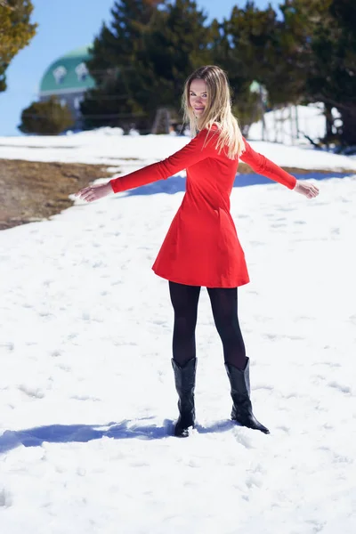 Donna che indossa un vestito rosso e calze nere aprendo le braccia nella felicità nelle montagne innevate. — Foto Stock