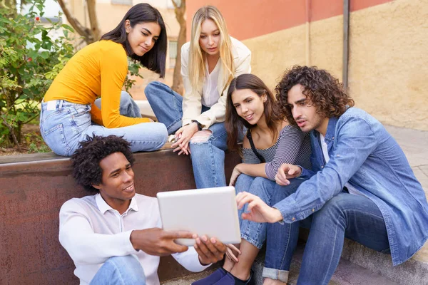 Multiethnische Gruppe junger Menschen, die im Freien vor urbanem Hintergrund ein digitales Tablet betrachten. — Stockfoto